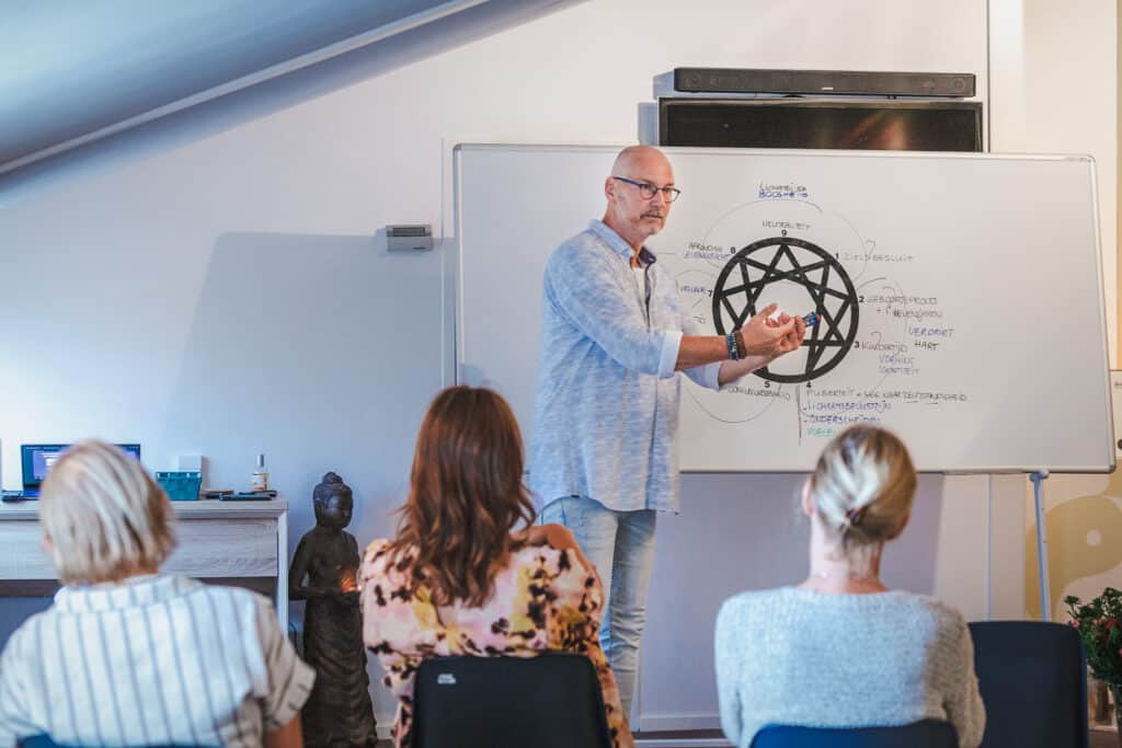 Trainer Marco neemt cursisten mee in de verdieping van het Enneagram met zijn beroemde tekeningen, terwijl hij voor een groep staat.
