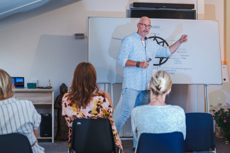 Trainer Marco neemt cursisten mee in de verdieping van het Enneagram met zijn beroemde tekeningen, terwijl hij voor een groep staat.