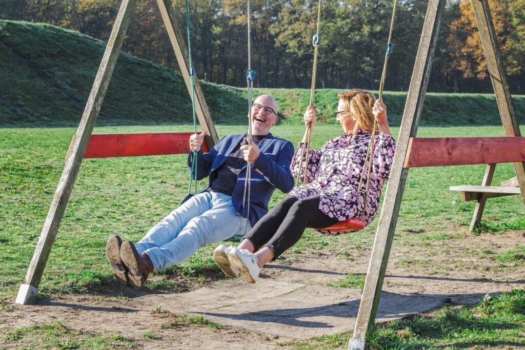 Trainers Marco en Jacquelien lachend op de schommel op een zomerse dag.