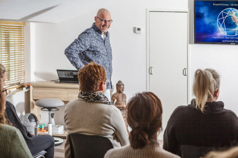Marco lachend voor de groep die hij les geeft in het breathfulness center