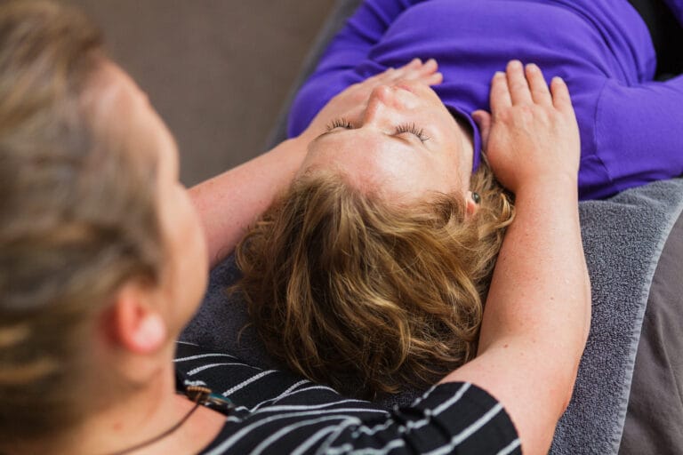 Coach helpt klant ontspannen door schouders vast te houden.